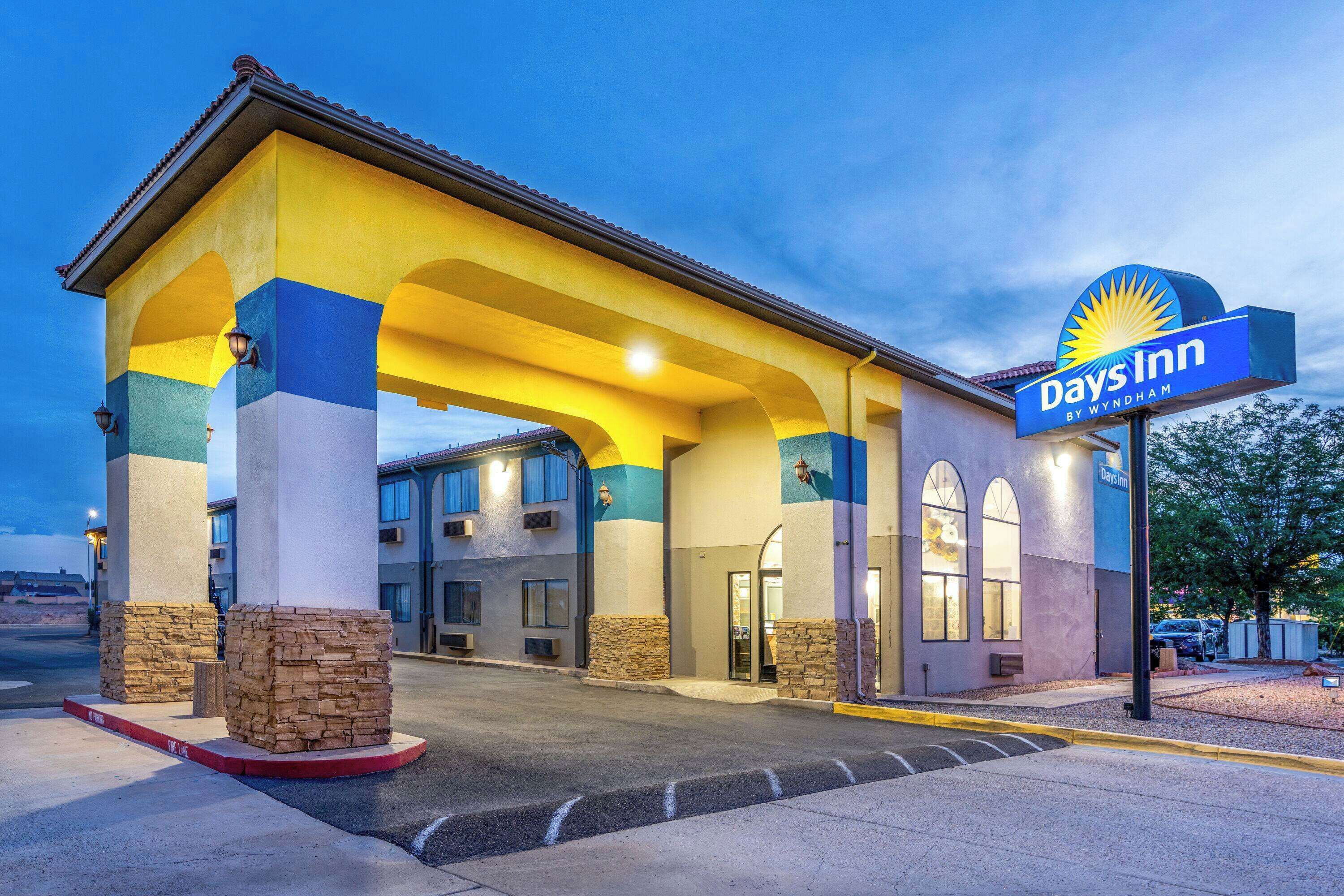 A Days Inn by Wyndham with a yellow and blue facade, stone pillars, and a covered entrance.