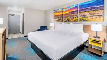 A hotel room with a large bed, a nightstand with a lamp, a wall-mounted painting, and a door leading to another room.