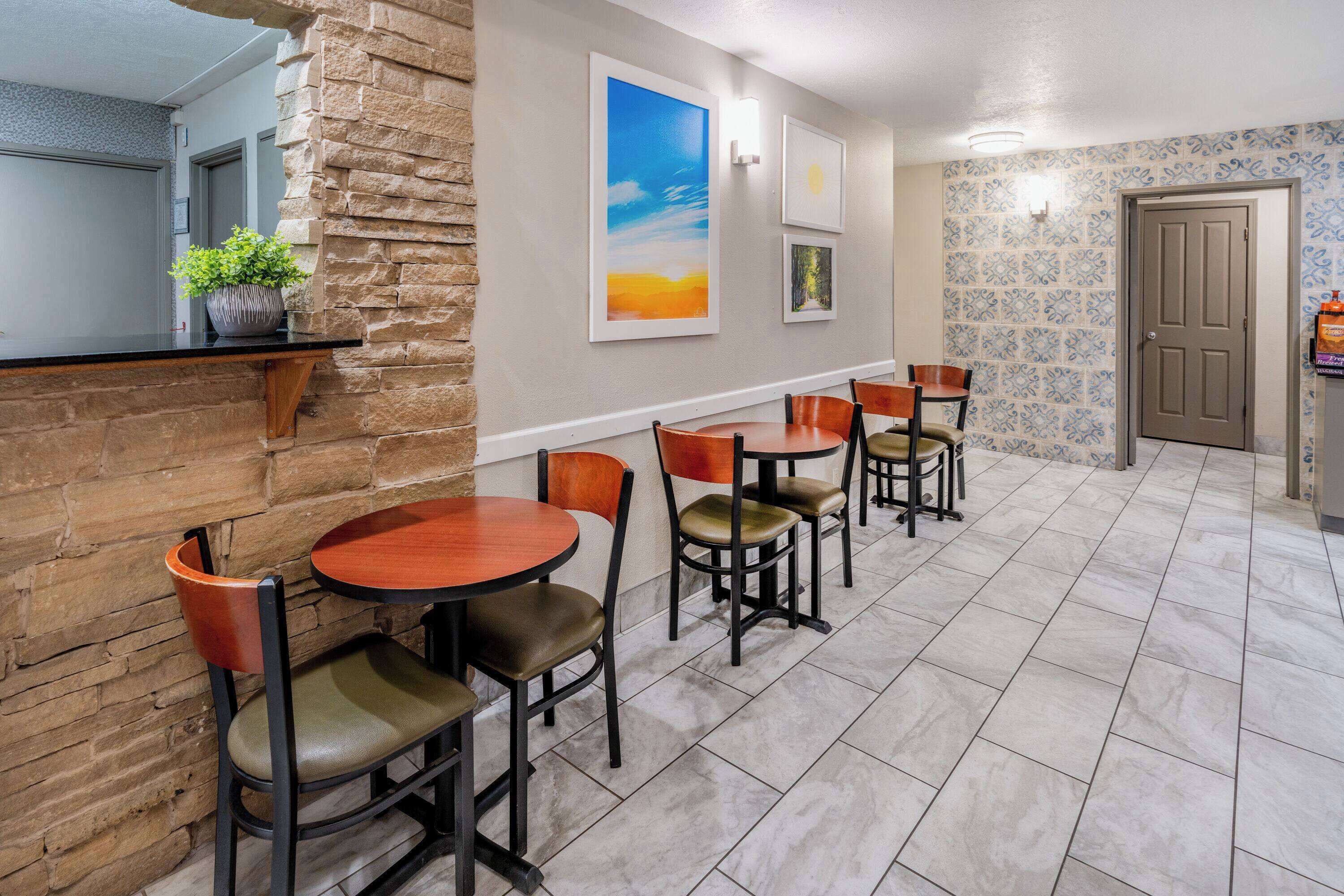 A hotel lobby with a stone wall, a reception desk, and a seating area with tables and chairs.