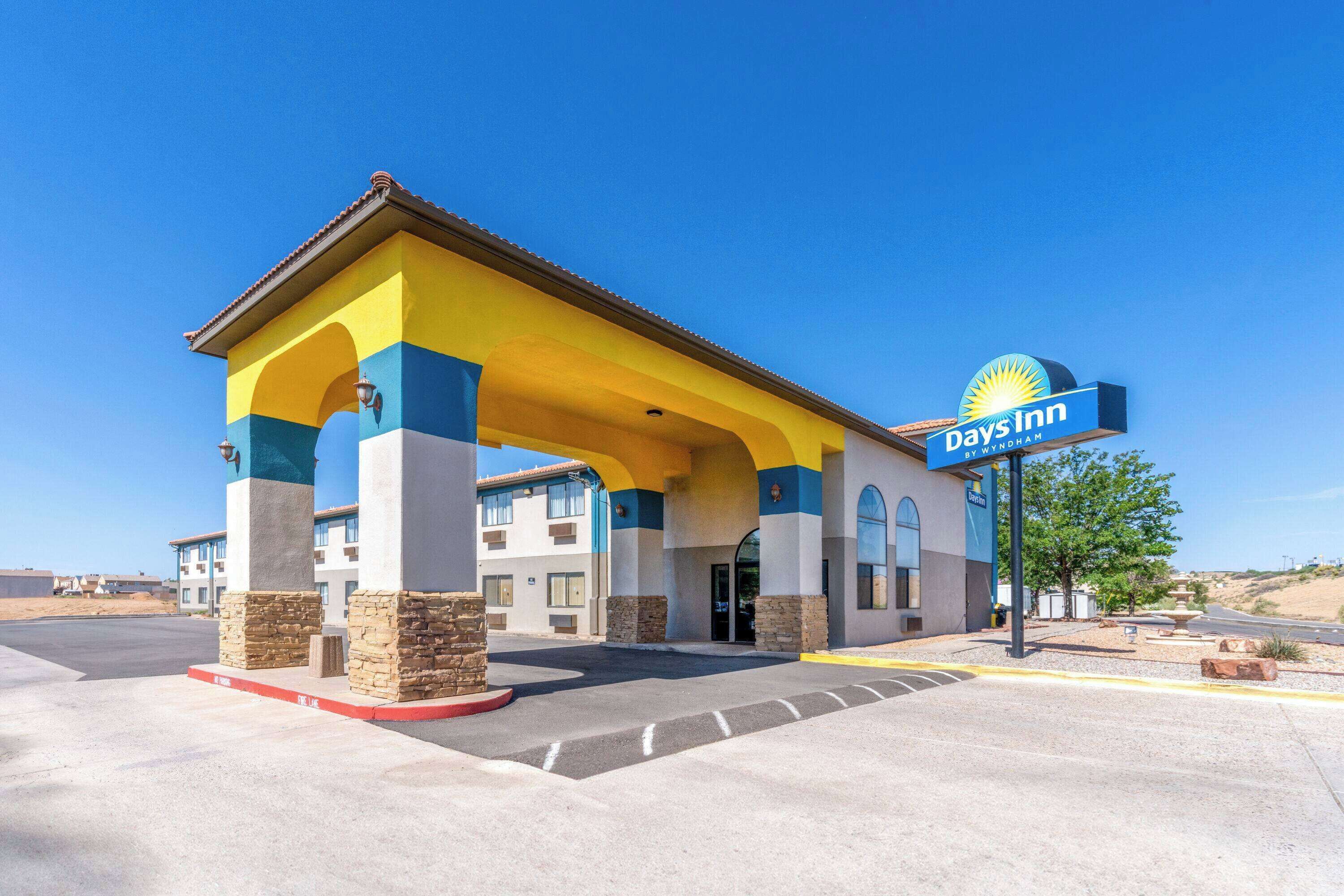 Un hotel Days Inn con fachada amarilla y azul, un cielo azul despejado y un estacionamiento.