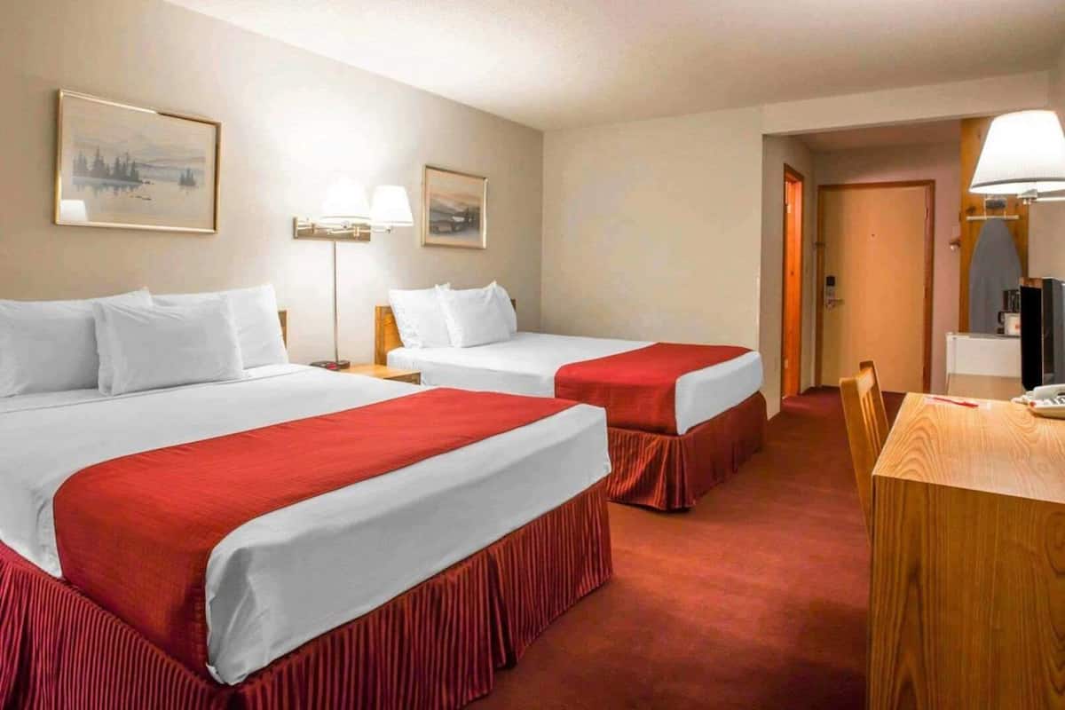 A hotel room with two beds, a desk, and a chair.