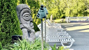 A stone sculpture, a row of white lounge chairs, and lush greenery. - Tiki Resort (Lake George)