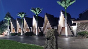 A modern building with a unique triangular roof design, surrounded by well-maintained lawns and palm trees.
