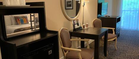 A hotel room with a bed, a desk, a chair, a television, a mirror, and a window with curtains.