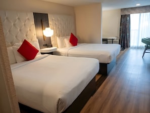 A hotel room with two beds, a nightstand, a lamp, and a view of the outside through a window. - Tiki Resort (Lake George)