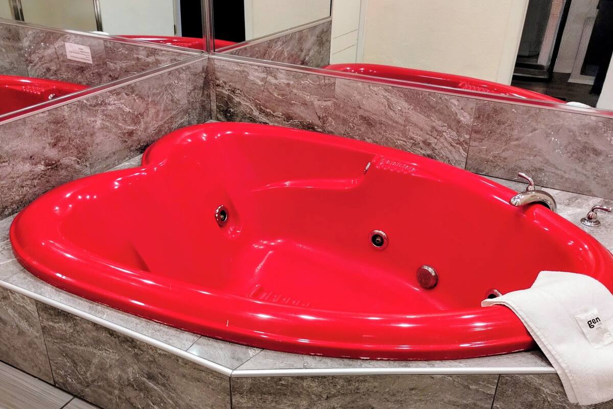 A red jacuzzi tub in a bathroom with marble tiles and a white towel on the side.
