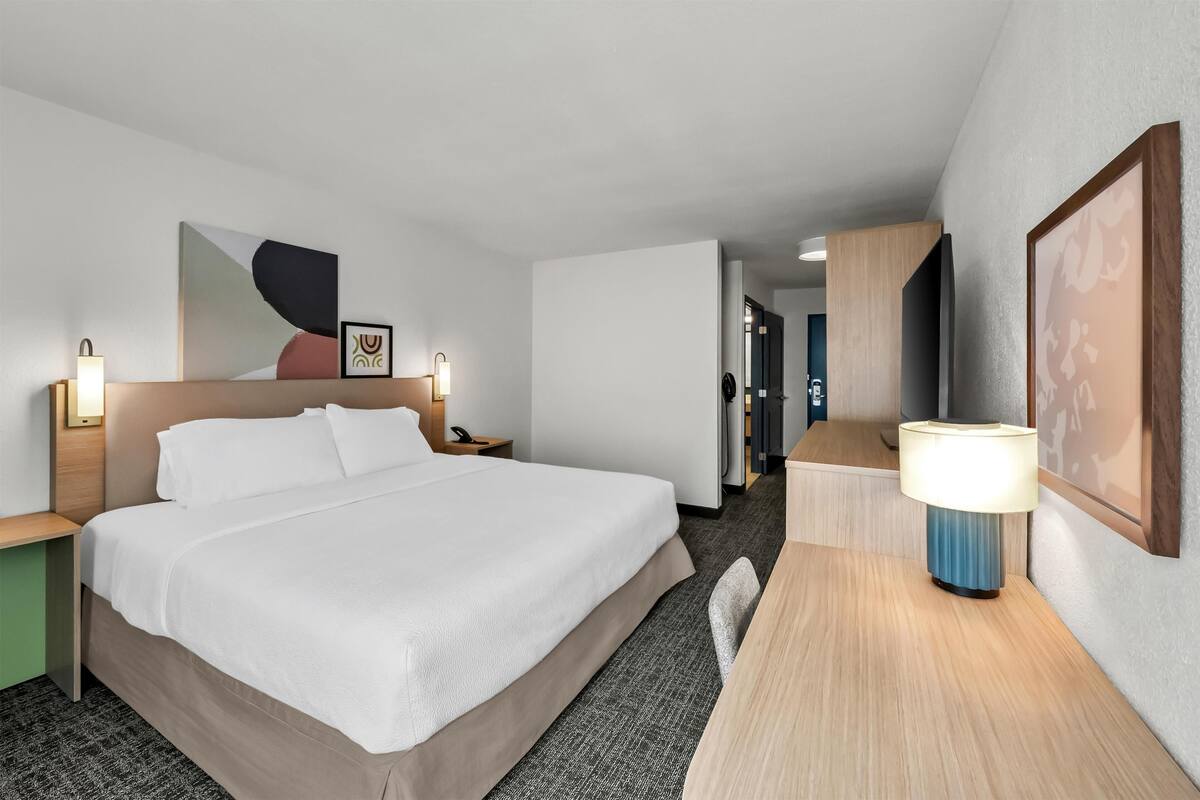 Une chambre d’hôtel avec un grand lit, des tables de chevet avec des lampes, un bureau et une chaise.