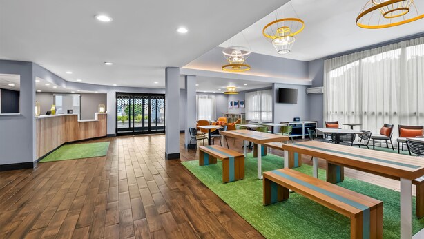 Une pièce spacieuse dotée d’un plancher en bois, d’une moquette verte et d’une longue table avec des bancs.