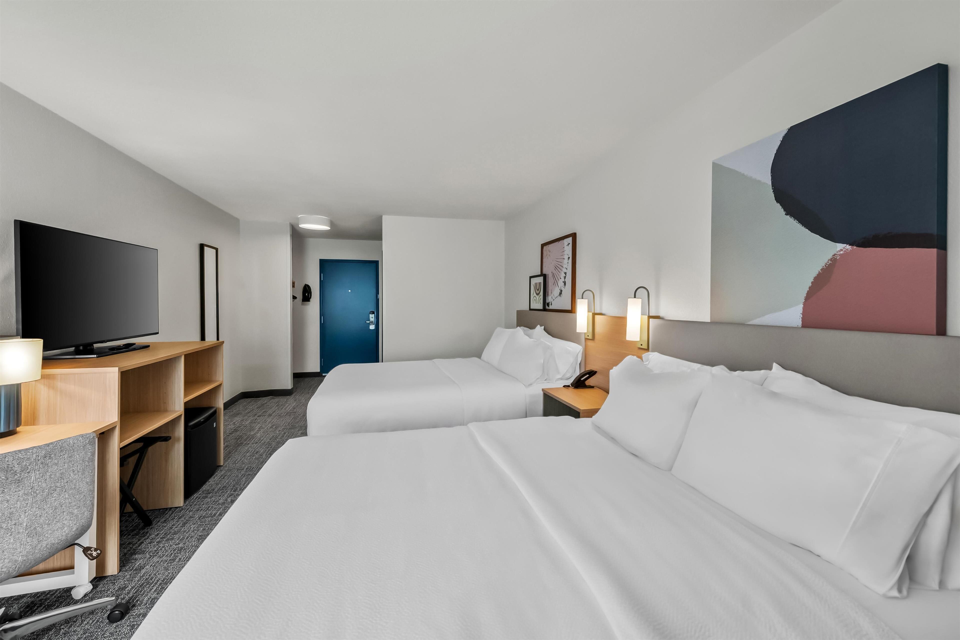 A hotel room with two beds, a desk with a TV, and a door leading to another room.