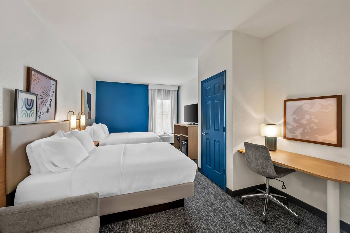 Une chambre d’hôtel avec deux lits, un bureau, une chaise, une télévision et une porte.