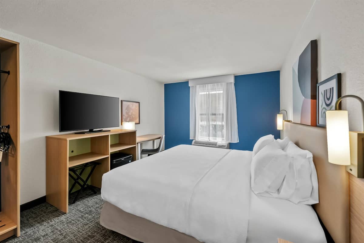 Une chambre d’hôtel avec un lit, un bureau, une télévision et une fenêtre avec des rideaux.