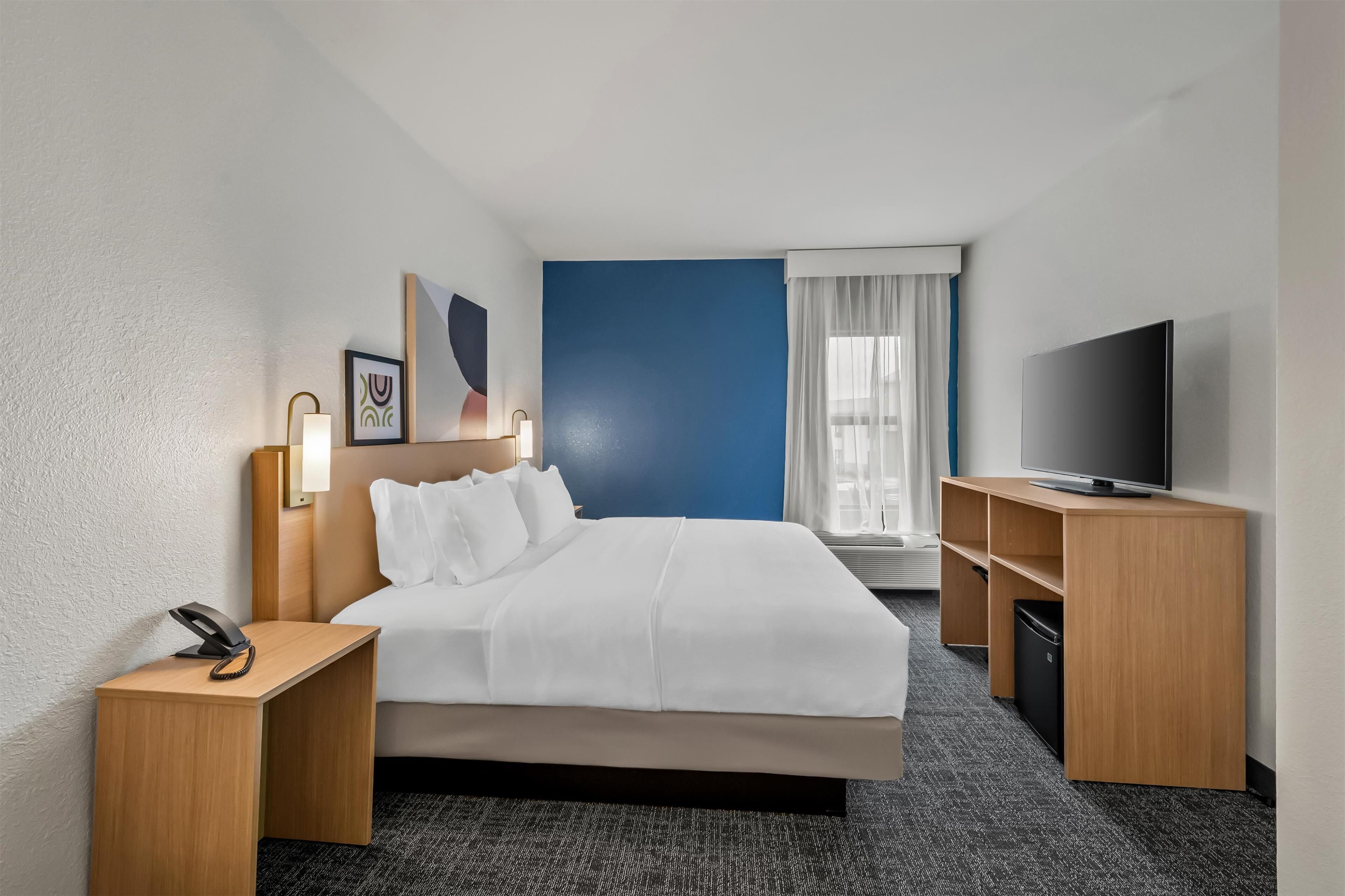 A hotel room with a bed, bedside tables, a TV, and a window with curtains.