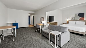 Une chambre d’hôtel comprenant un lit, un canapé, un bureau avec une lampe, une télévision et une petite kitchenette.