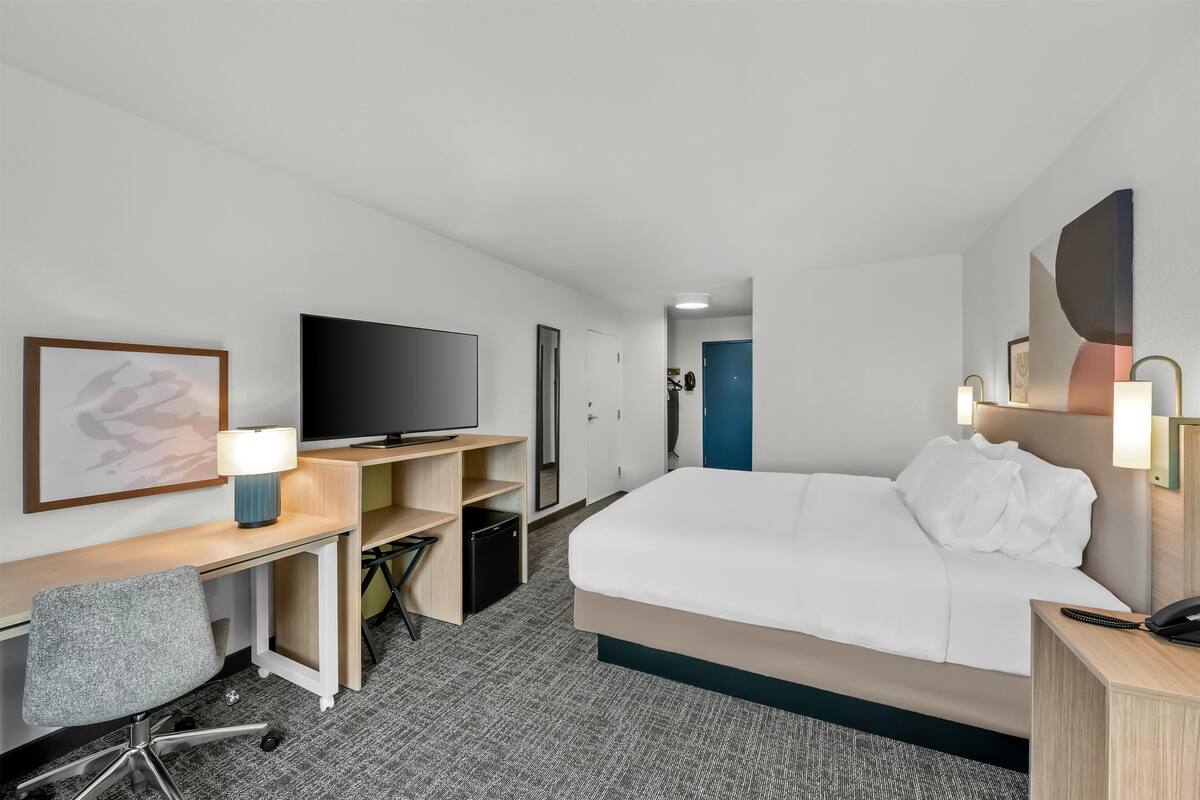 Une chambre d’hôtel comprenant un lit, un bureau, une chaise, une télévision et une porte donnant sur une autre pièce.