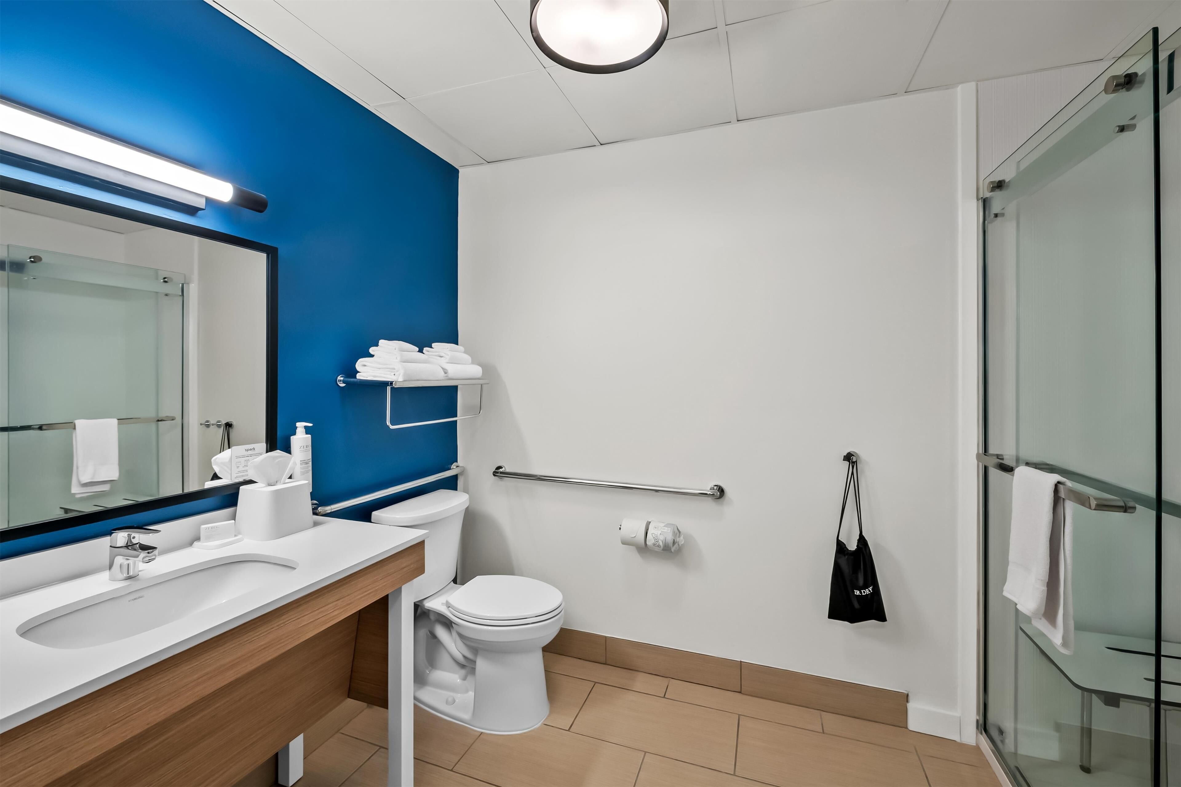 Un bagno moderno con un lavandino bianco, un water, cabina doccia in vetro e una parete d'accento blu.