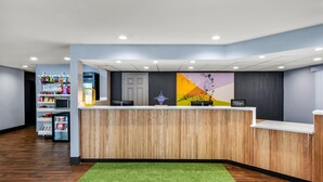 Un espace d’accueil d’hôtel avec un comptoir en bois, une moquette verte et un mur orné d’un motif abstrait et coloré.
