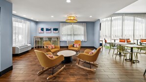 Un espace de restauration moderne avec un plancher en bois, des chaises jaunes, une table ronde centrale et de grandes fenêtres ornées de rideaux légers.