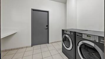 Un lavadero con dos lavadoras de carga frontal, una puerta gris y una pared blanca.