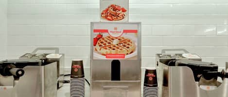 A waffle station with instructions and a dispenser, surrounded by stainless steel equipment.