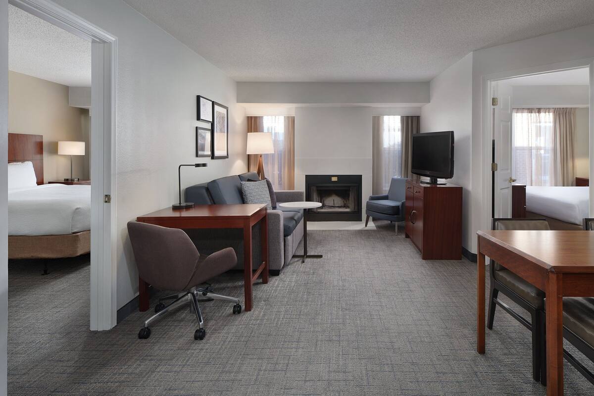 A hotel room with a bed, a sofa, a desk, a TV, and a fireplace.