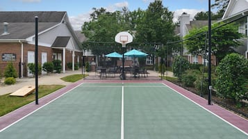 An outdoor basketball court with a net, surrounded by a fence, and adjacent to a building with a brick facade.