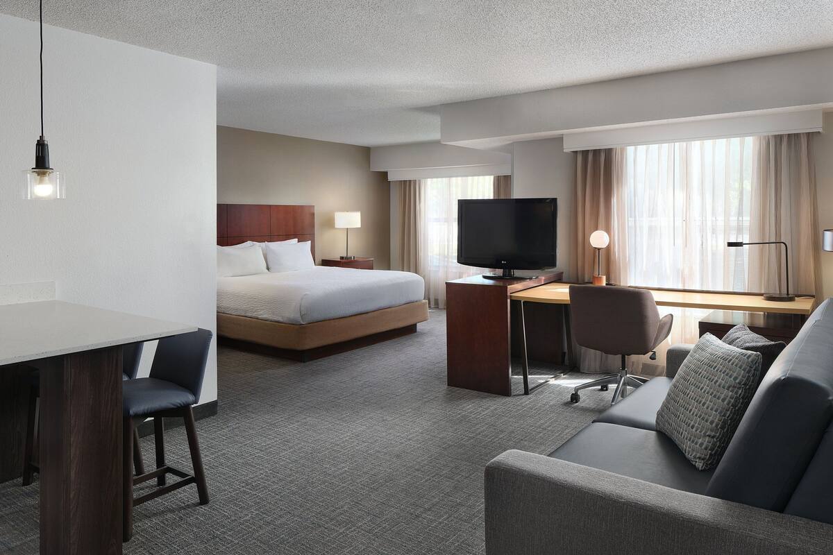 A hotel room with a bed, desk, TV, and seating area.