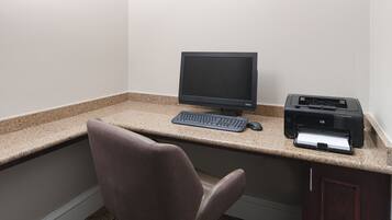 A small office space with a desktop computer, keyboard, mouse, and printer on a granite countertop.