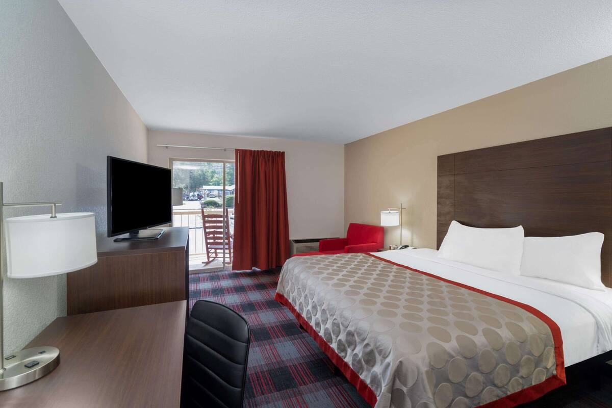 Une chambre d’hôtel avec un lit, un bureau avec une télévision, une chaise et une fenêtre avec des rideaux.