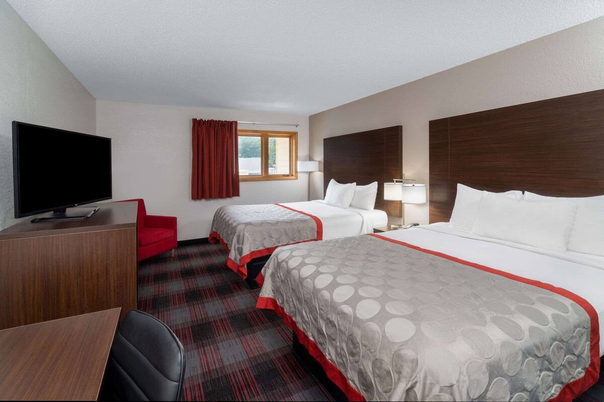 Une chambre d’hôtel avec deux lits, une télévision, un bureau et une chaise rouge.