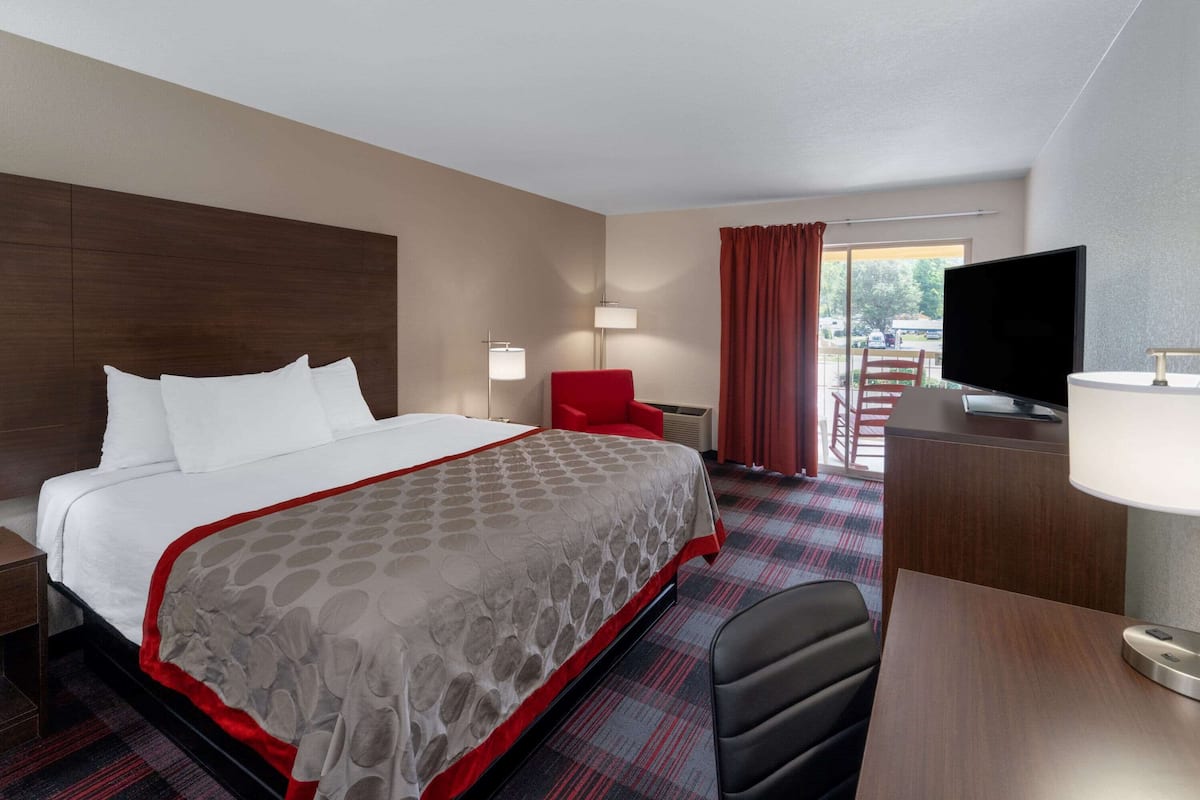 Une chambre d’hôtel avec un grand lit, un bureau, une chaise, une télévision et une fenêtre avec des rideaux.