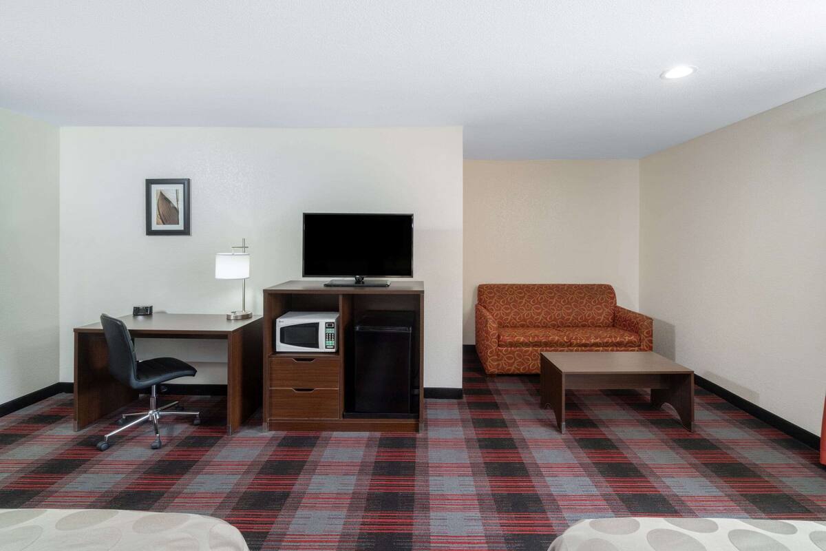 Une chambre d’hôtel équipée d’un bureau, d’une télévision, d’un four à micro-ondes, d’une moquette à motifs et d’un fauteuil à motifs.