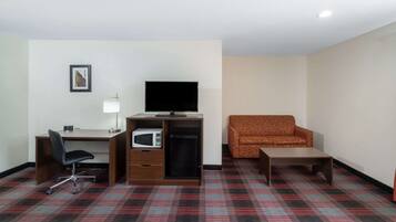 Habitación de hotel con escritorio, televisión, microondas, alfombra estampada y sillón estampado.