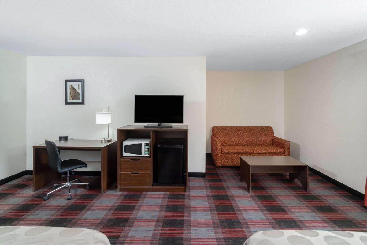 Une chambre d’hôtel équipée d’un bureau, d’une chaise, d’une télévision, d’un micro-ondes, d’un canapé et d’une petite table.