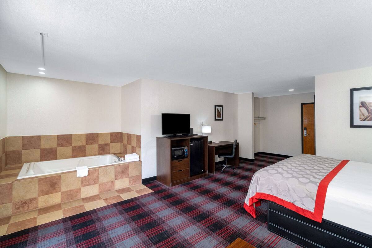 Une chambre d’hôtel avec un sol à carreaux, un lit, un bureau, une télévision, un four à micro-ondes et une baignoire.