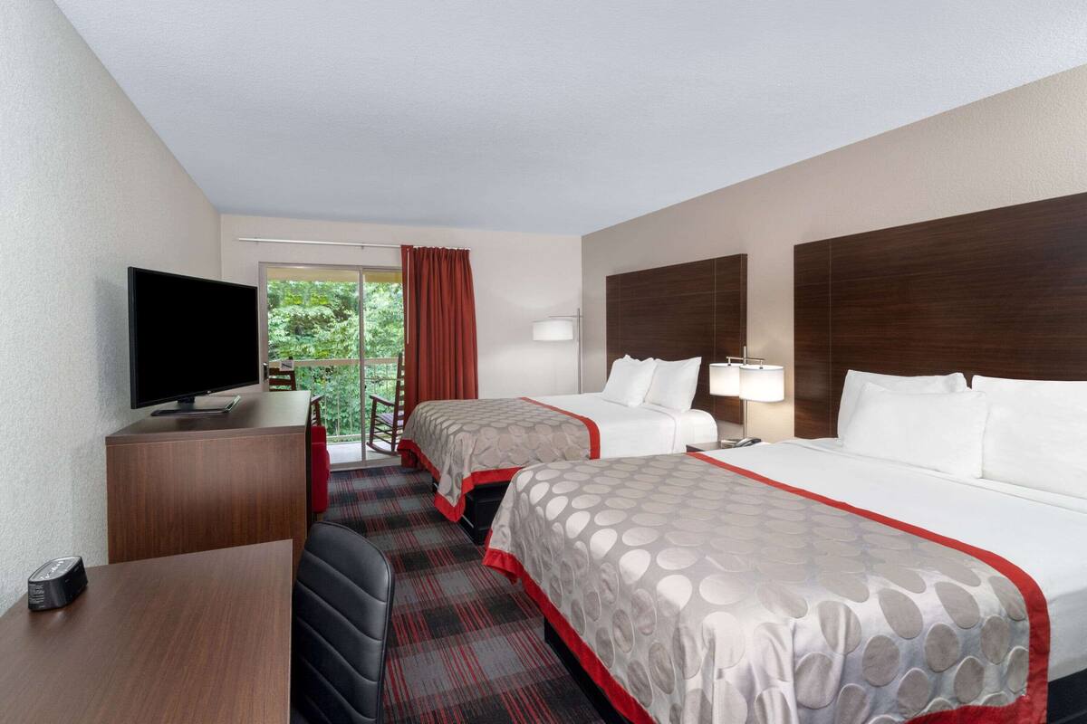 Une chambre d’hôtel avec deux lits, un bureau avec une télévision, une lampe et une vue sur la verdure environnante.