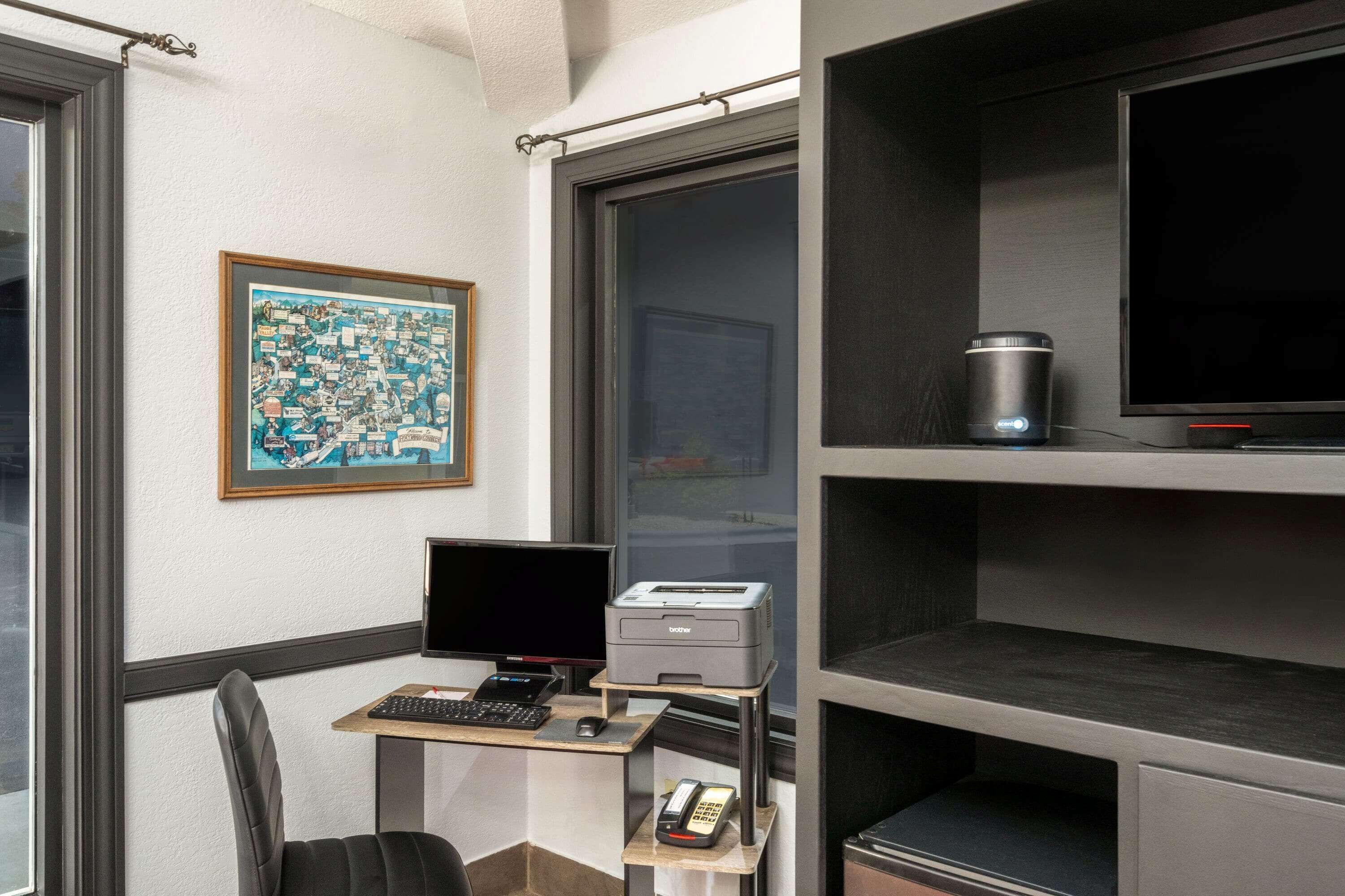 A modern office space with a desk, computer, printer, and a large window.