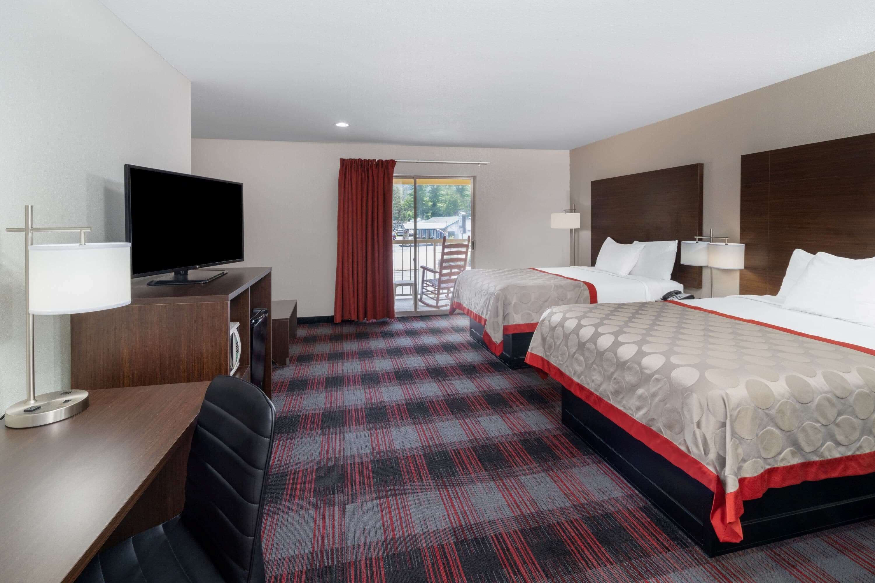 A hotel room with two beds, a desk with a TV, a chair, and a view of the outdoors.