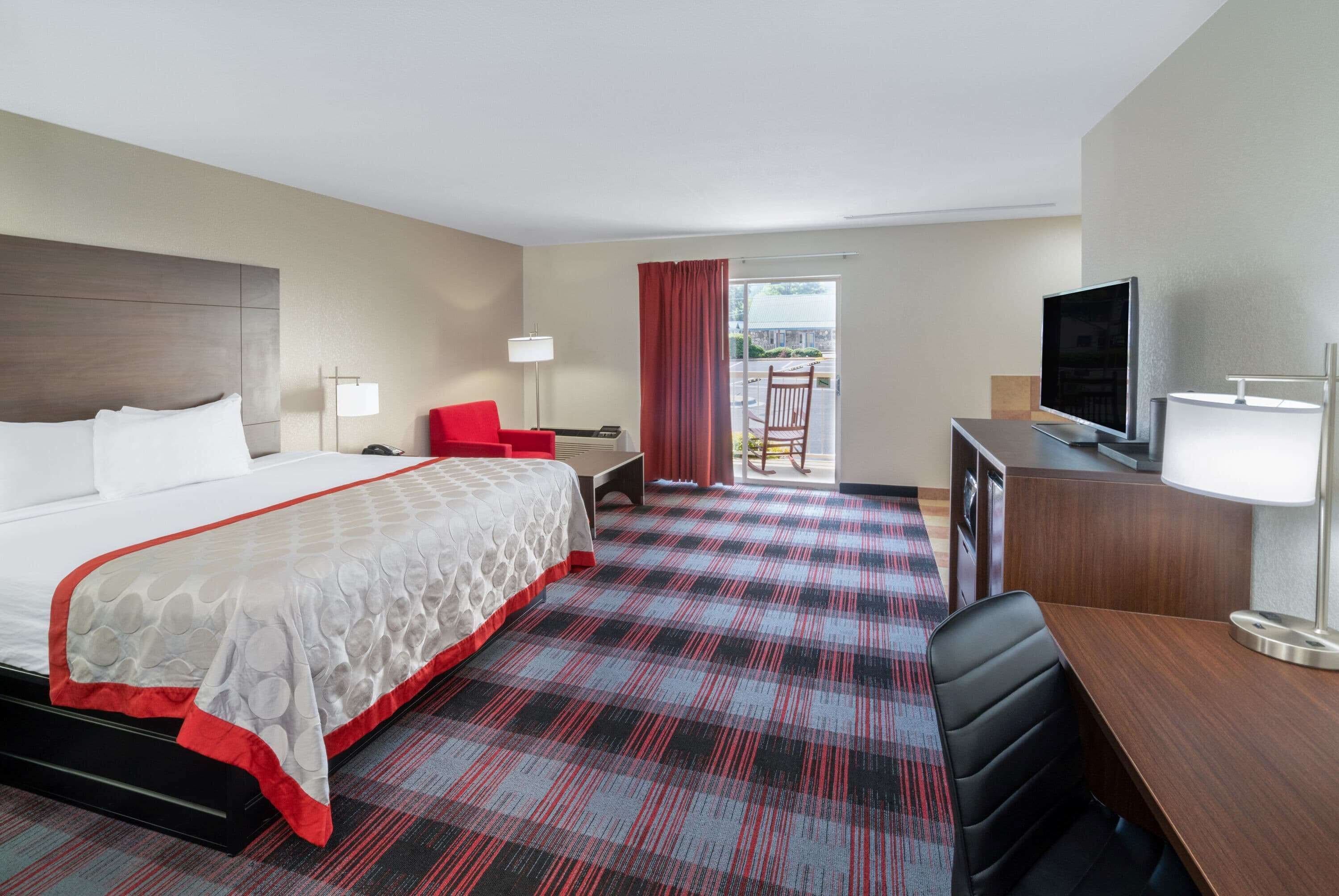 A hotel room with a large bed, a desk with a TV, a chair, and a view of the outdoors.