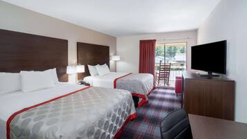 A hotel room with two beds, a TV, a desk, and a view of the outdoors.