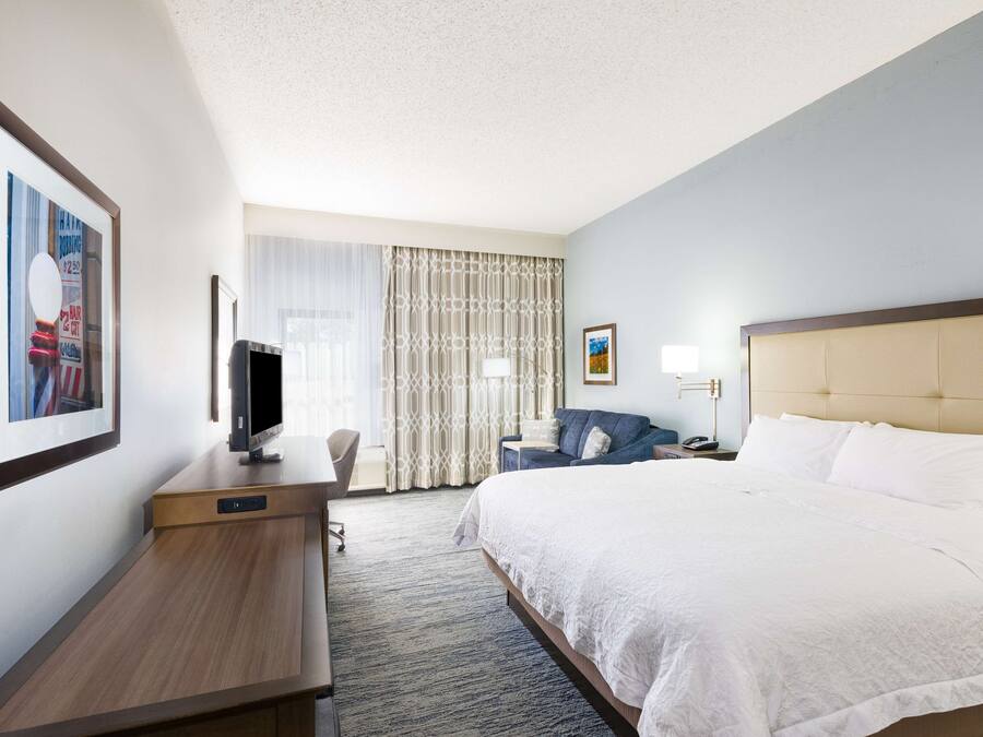 A hotel room with a bed, a desk, a television, and a window with curtains.