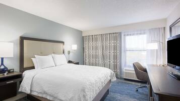 A hotel room with a large bed, a desk, a chair, a TV, and a window with curtains.