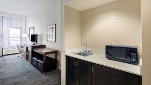 Une chambre d’hôtel équipée d’une kitchenette, d’un bureau avec une chaise, d’une télévision et d’une fenêtre avec des rideaux.