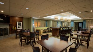 Un hall d’hôtel doté de plusieurs tables et chaises, d’une cheminée et d’un téléviseur.