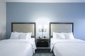 A hotel room with two beds, a nightstand with a lamp, and a wall-mounted light fixture.