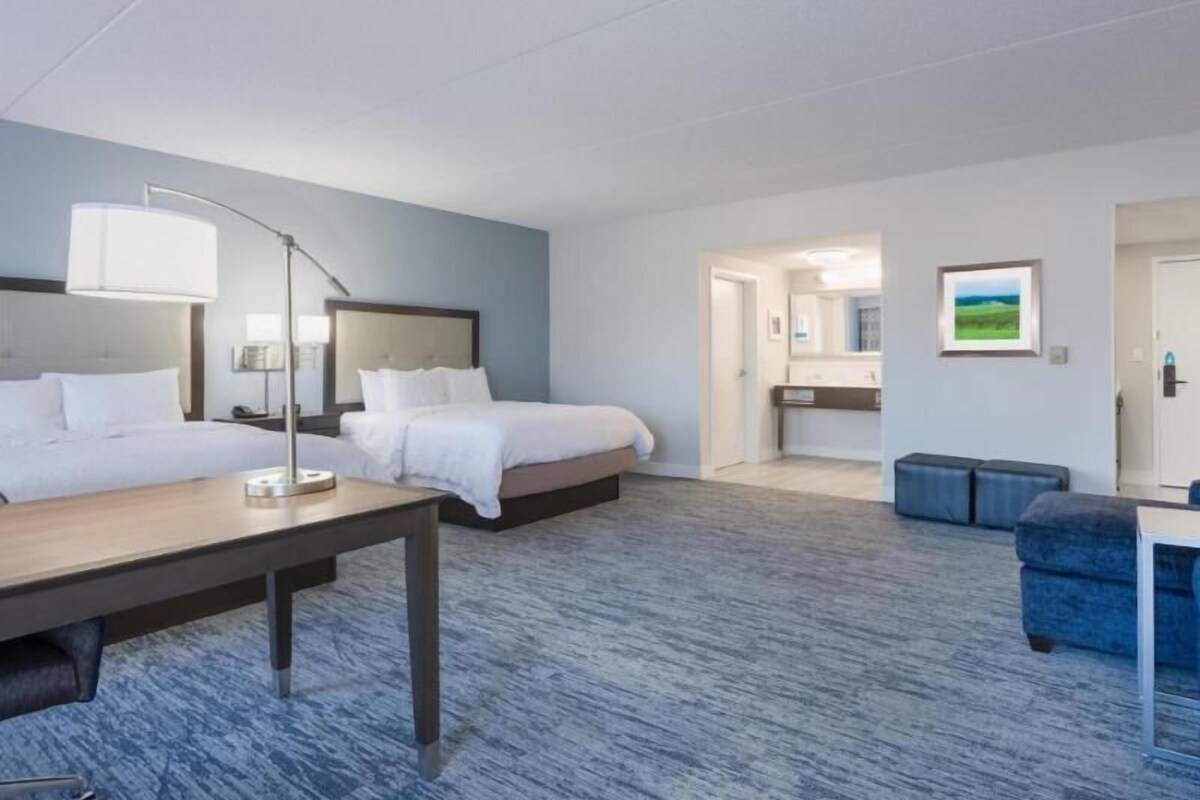 Habitación de hotel con dos camas, un escritorio, una silla, un sofá, un baño y un pasillo.