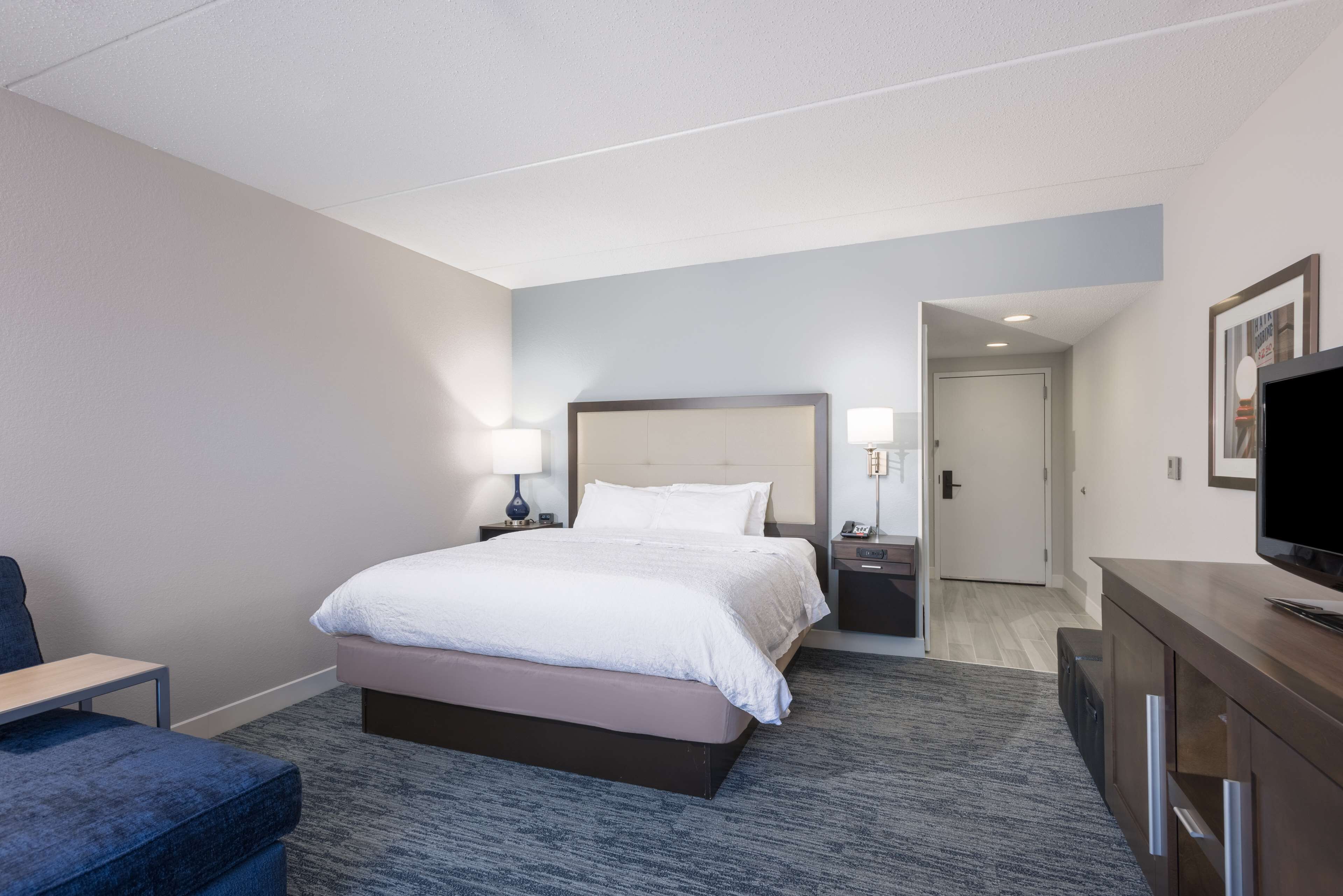 Une chambre d’hôtel comprenant un lit, des tables de chevet, un bureau, une chaise, une télévision et une porte donnant sur une autre pièce.