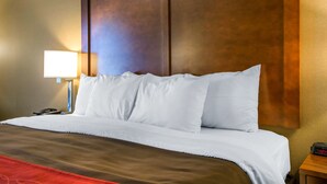 Quarto de hotel com uma cama grande, cabeceira de madeira, abajur e relógio digital.