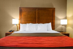 Une chambre d’hôtel avec un grand lit, deux lampes de chevet, un téléphone et un téléviseur posés sur une table de chevet en bois.