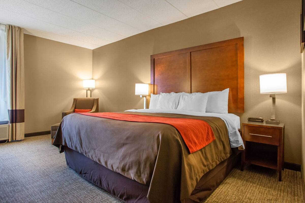 A hotel room with a large bed, two bedside tables with lamps, a chair, and a window with curtains.