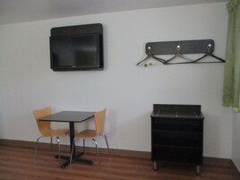 Una habitación pequeña con un televisor montado en la pared, una mesa con dos sillas y un mueble de almacenamiento negro.